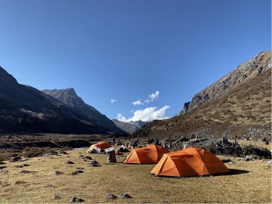 Trekking camp with orange tents in a high Himalayan valley