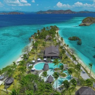 Aerial view of an island resort with pools and thatched pavilions on the reef edge