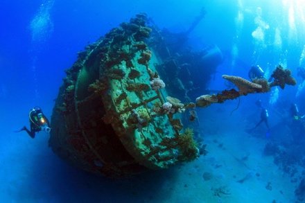 Divers beside the bow of a large upright wreck in blue water