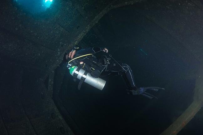 Diver with a torch inside the dark hold of a sunken ship
