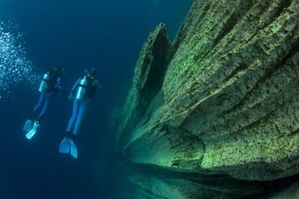 Two divers finning along the encrusted hull of a sunken ship