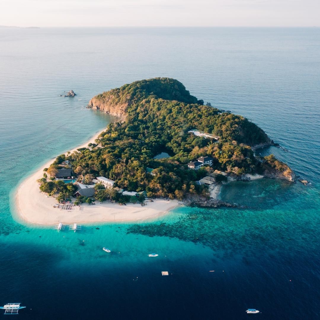 Aerial view of a private island resort ringed by white sand and turquoise reef, Palawan