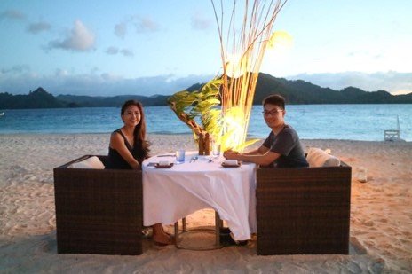 Couple at a candlelit table set on the sand at dusk