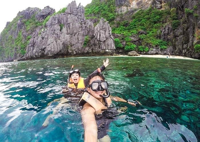 Snorkellers in clear water below the karst cliffs of Bacuit Bay