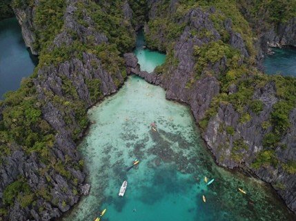 Aerial view of kayaks entering a hidden lagoon between limestone cliffs