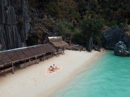 Couple at a private beach picnic beneath a thatched shelter