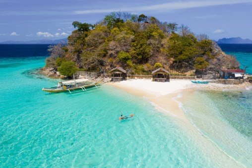 Swimmer in shallow turquoise water off a palm-covered islet