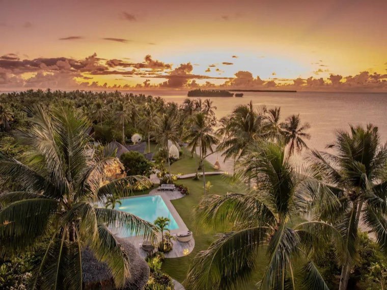 Resort pool and gardens among coconut palms at sunset above the Pacific