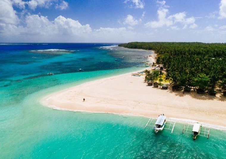 Aerial view of a white sandbar edged by turquoise water with outrigger boats moored offshore