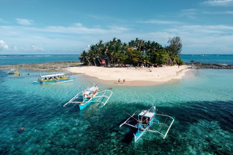 Outrigger bangka boats anchored off a small palm island with a white-sand spit