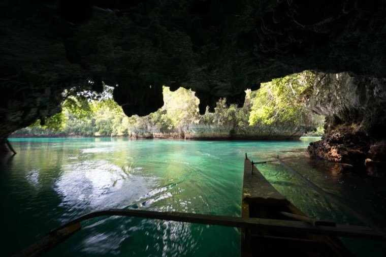 View from a boat inside a sea cave looking out to a green lagoon