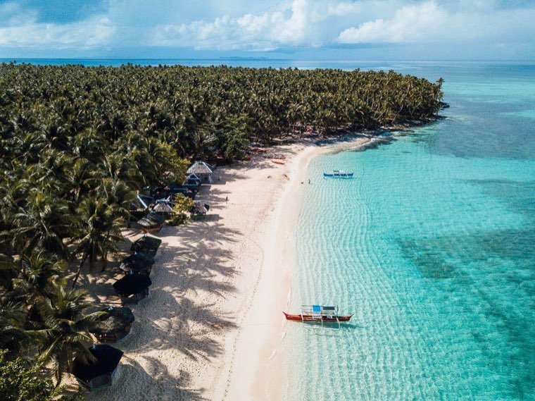 Palm-lined white-sand beach with an outrigger boat in shallow turquoise water
