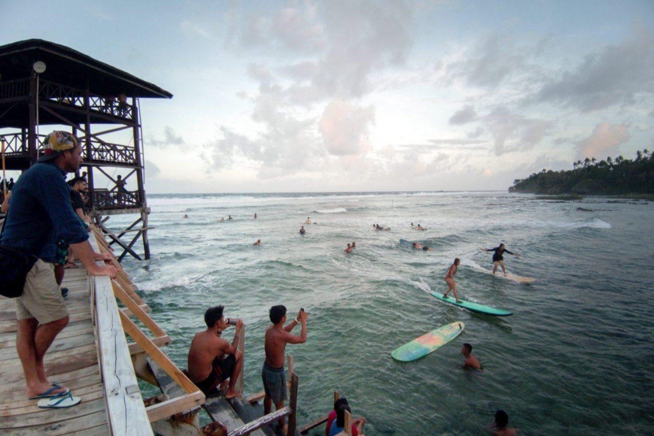 Surfers on the wave at Cloud 9, Siargao, watched from the boardwalk tower at sunset